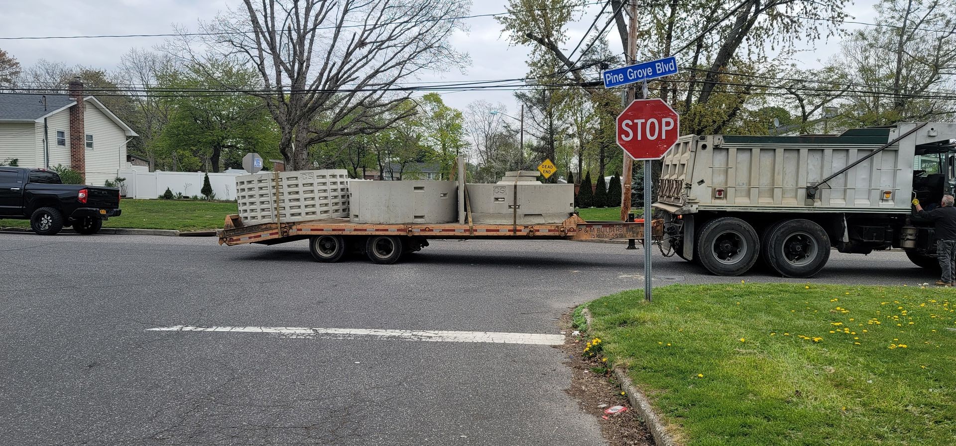 Flatbed truck carrying concrete structures at an intersection with stop and dead-end signs.